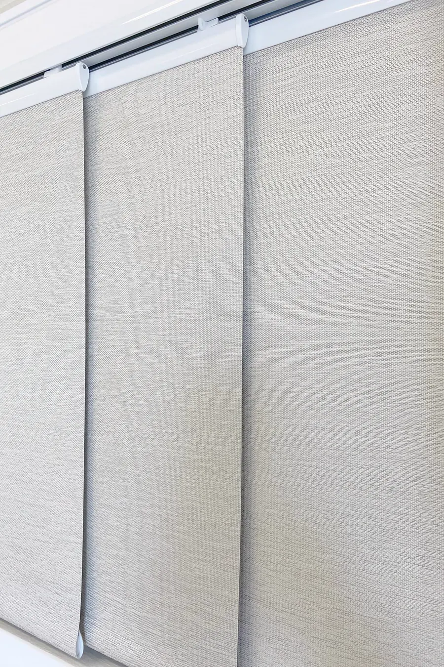 Close-up of light grey panel glide blind fabric panels suspended from a multi-channel track