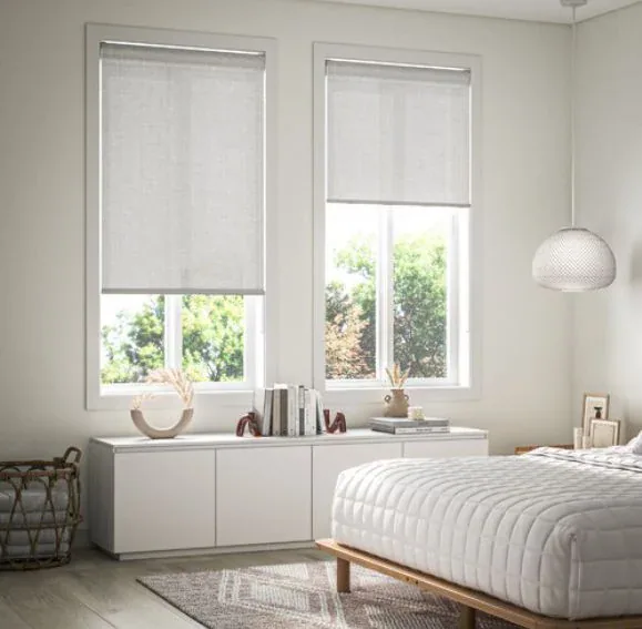 Two light-filtering roller blinds softly diffusing daylight in a bright bedroom