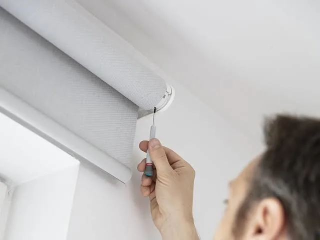 Installer securing a roller blind bracket at a window
