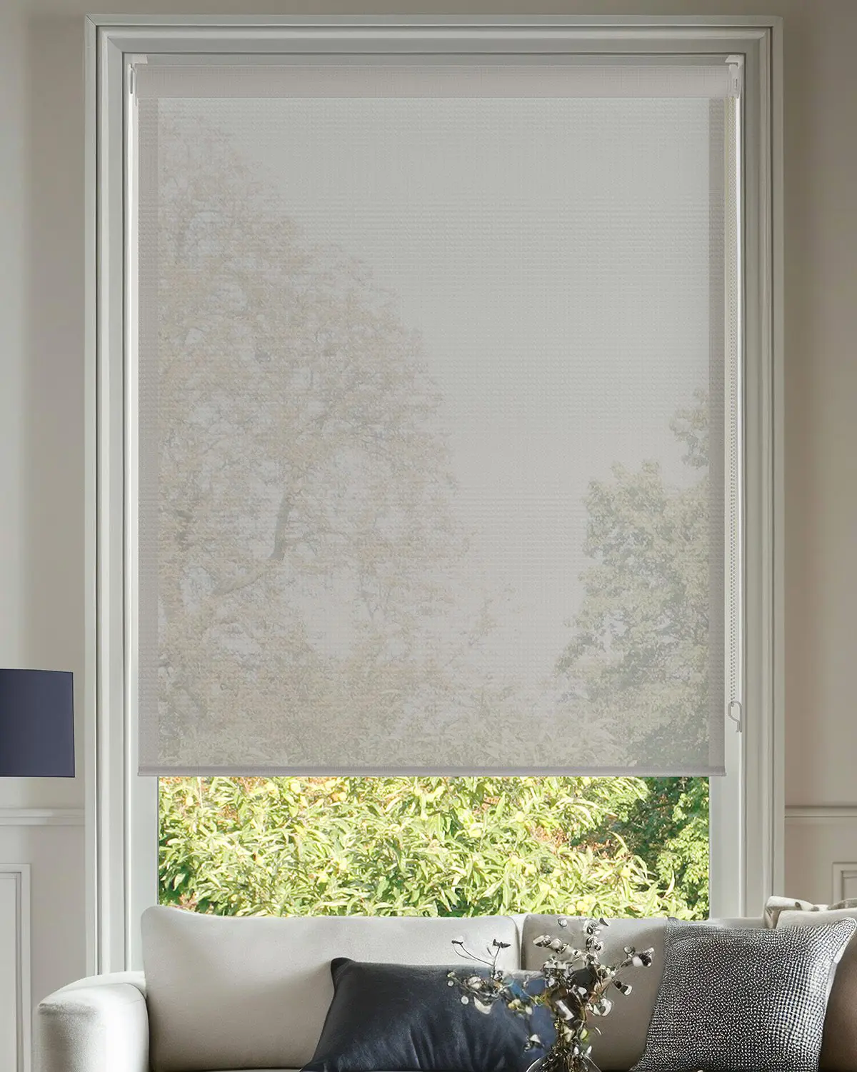 White light-filtering roller blind softly screening daylight above a living room sofa