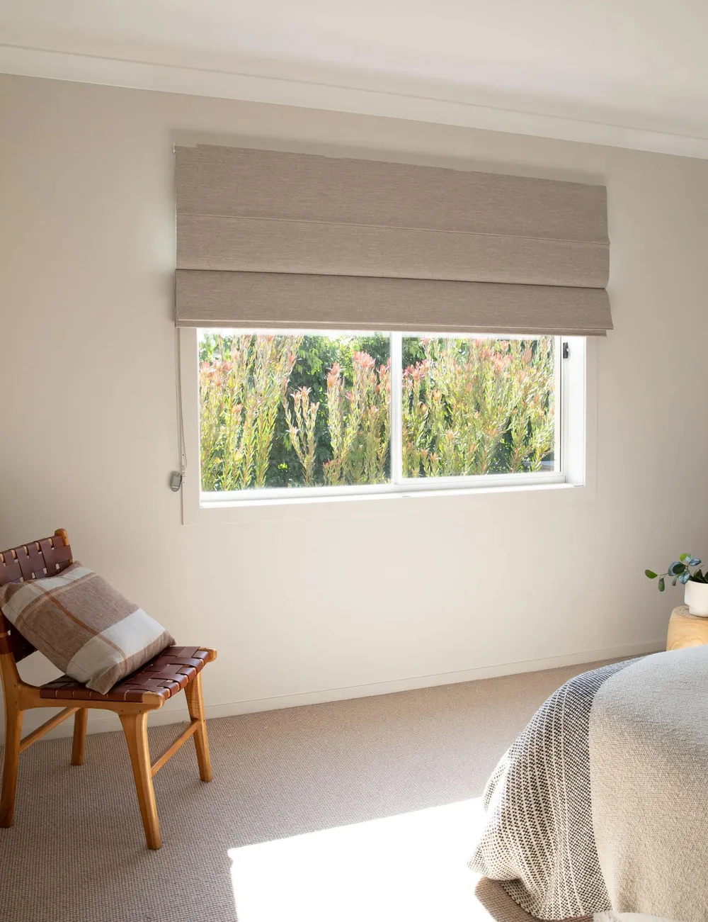 Taupe Roman blind partially raised above a bright bedroom window