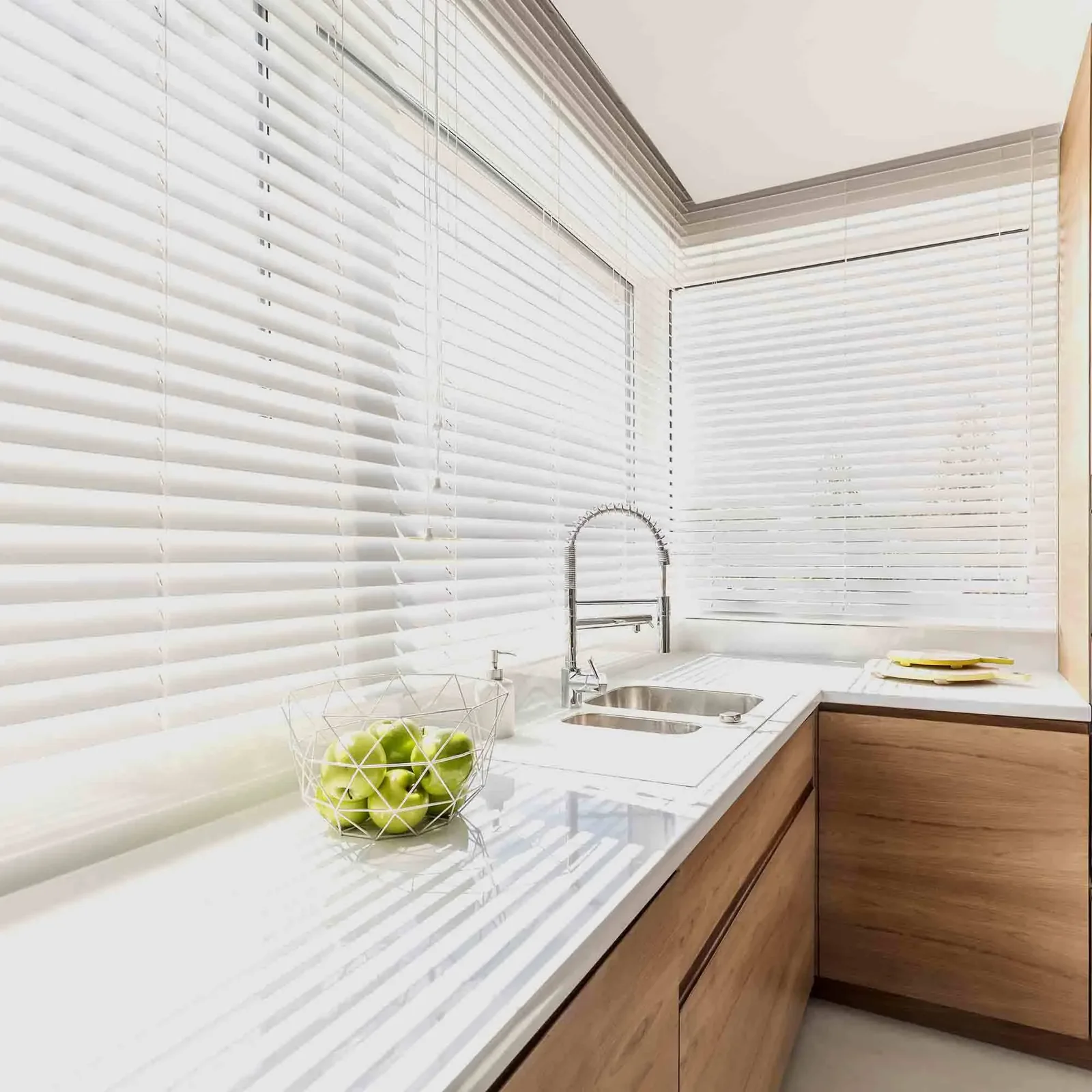 White Venetian blinds fitted across corner kitchen windows above a timber benchtop