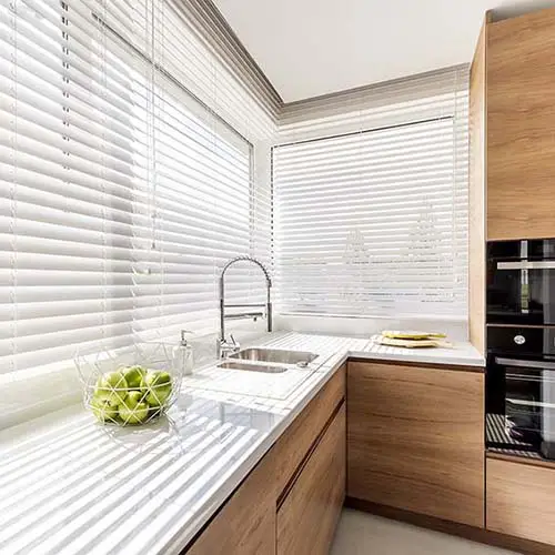 White Venetian blinds over a modern kitchen window with a minimalist benchtop setup